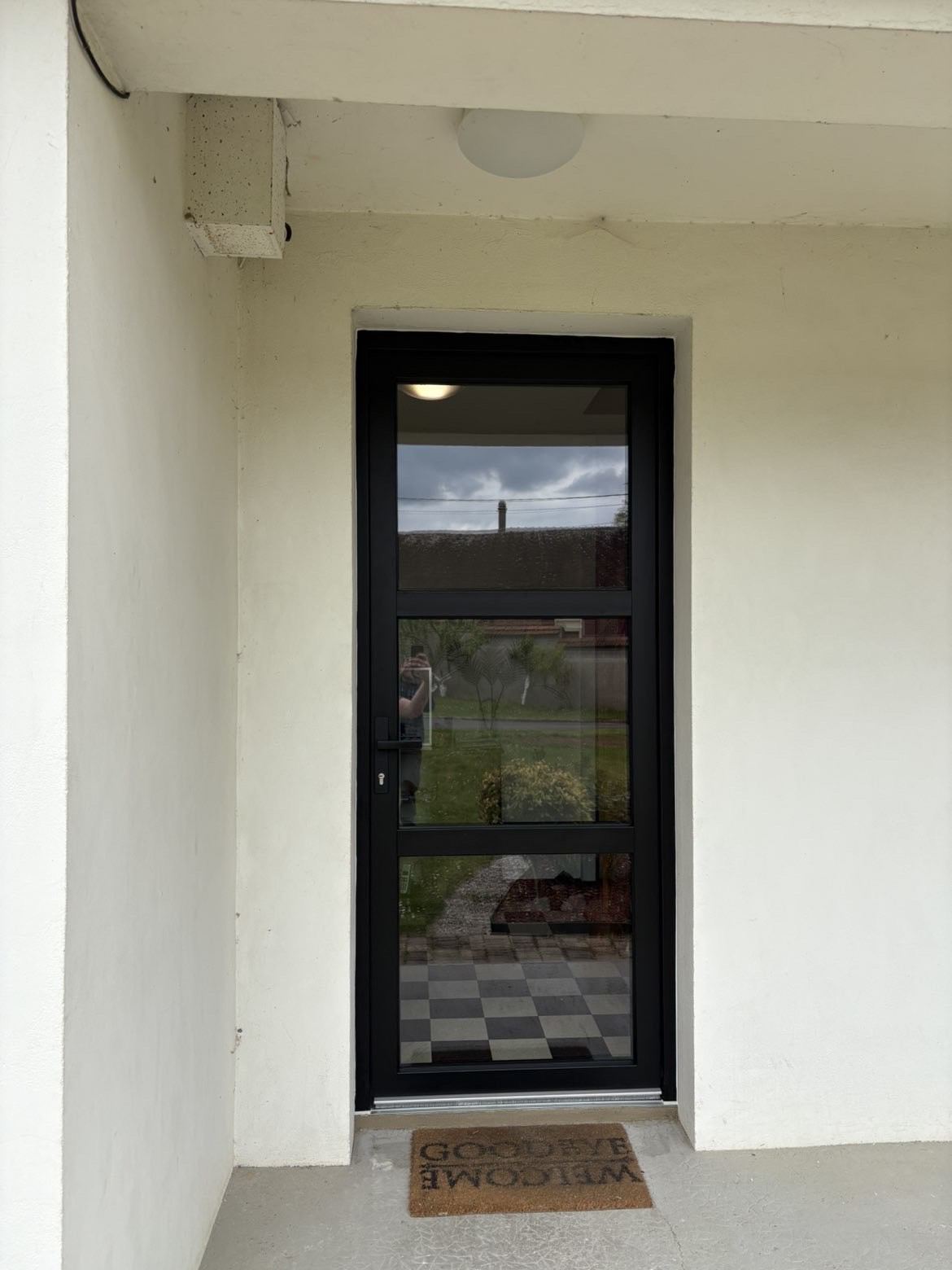 Porte d'entrée entièrement vitrée à cadre aluminium noir, posée sous un porche