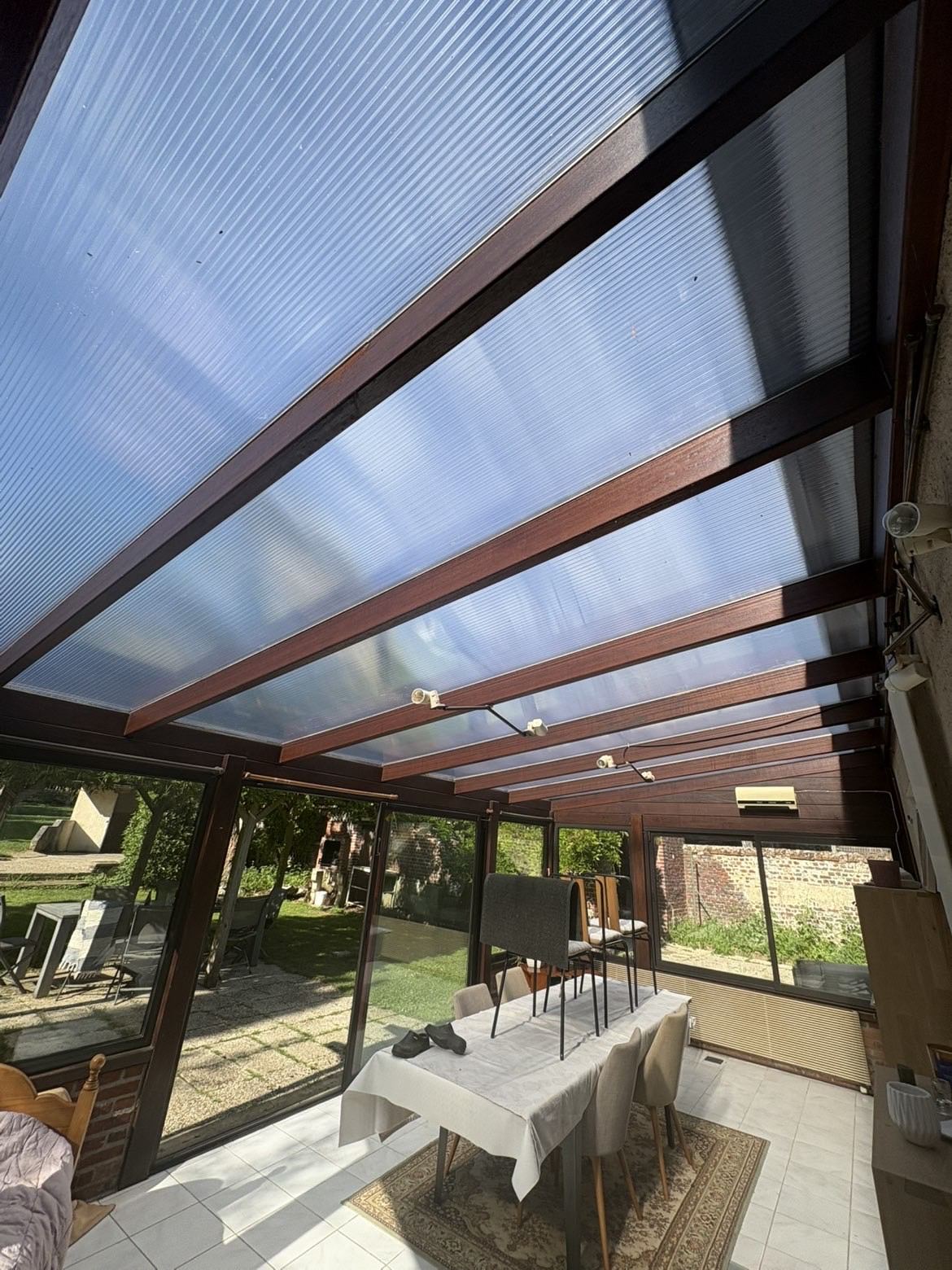 Intérieur d'une véranda à structure bois et toiture translucide donnant sur le jardin